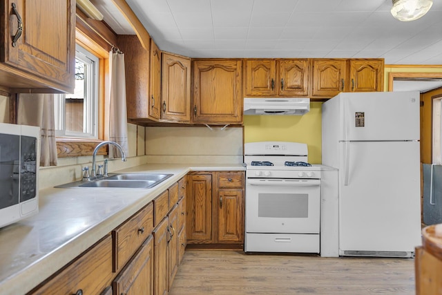 kitchen featuring under cabinet range hood, white appliances, brown cabinetry, and a sink