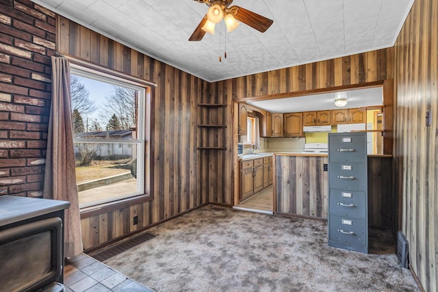 kitchen featuring under cabinet range hood, wood walls, light countertops, brown cabinetry, and a sink