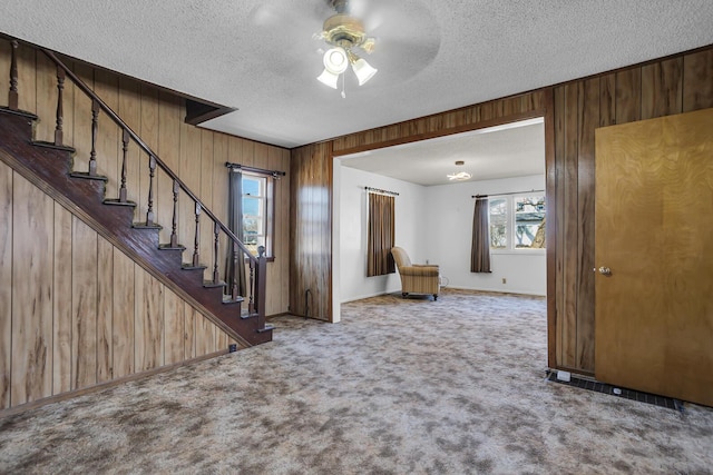 carpeted foyer entrance featuring baseboards, stairway, wood walls, a textured ceiling, and a ceiling fan