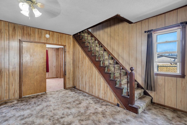 stairway featuring wooden walls, a textured ceiling, and carpet