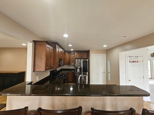 kitchen featuring dark stone counters, recessed lighting, a peninsula, black electric range, and stainless steel fridge