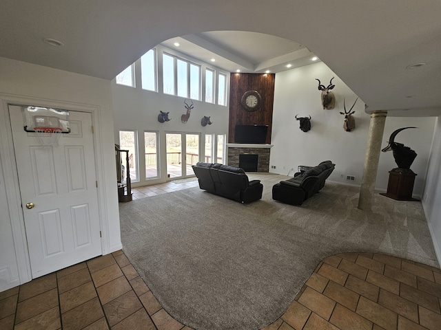 unfurnished living room with carpet floors, arched walkways, a stone fireplace, tile patterned flooring, and a towering ceiling