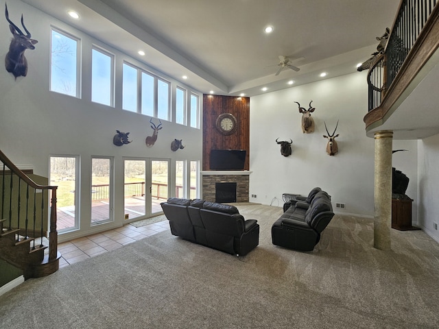 living area featuring a ceiling fan, a high ceiling, a stone fireplace, stairs, and carpet flooring