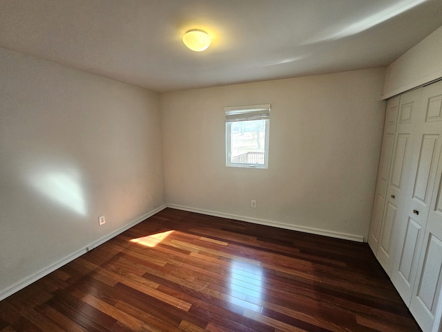 unfurnished bedroom featuring dark wood-style floors, a closet, and baseboards