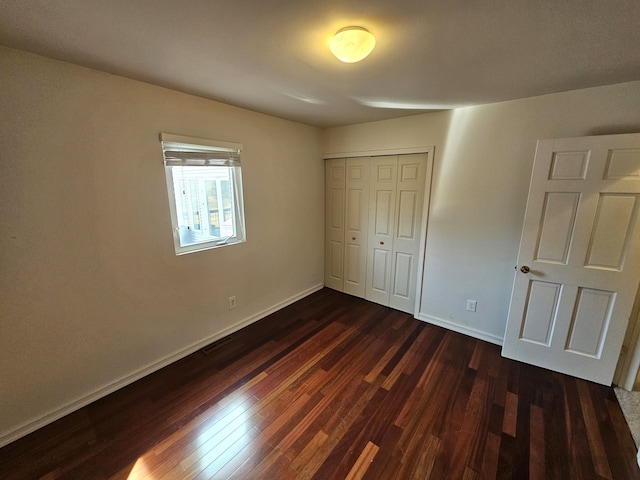 unfurnished bedroom with a closet, baseboards, and dark wood-style flooring