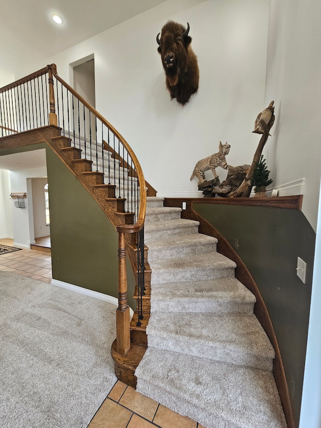 stairway featuring tile patterned floors, baseboards, carpet, and a towering ceiling