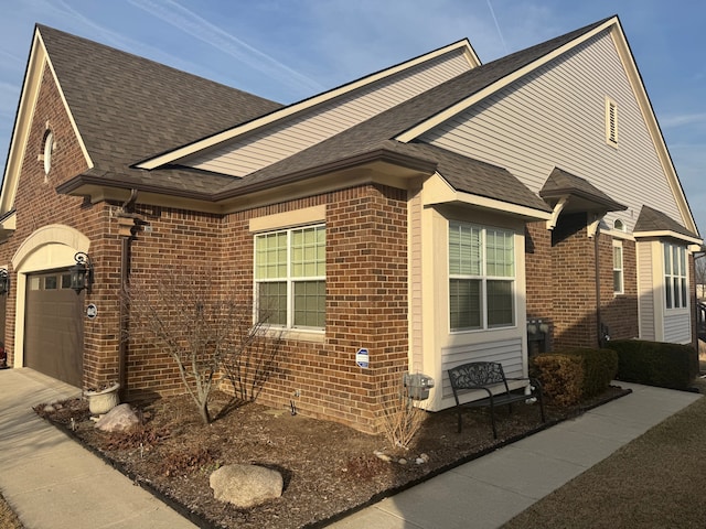 view of side of home with brick siding, concrete driveway, and a shingled roof