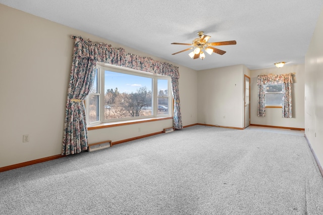 carpeted spare room with a textured ceiling, baseboards, visible vents, and ceiling fan