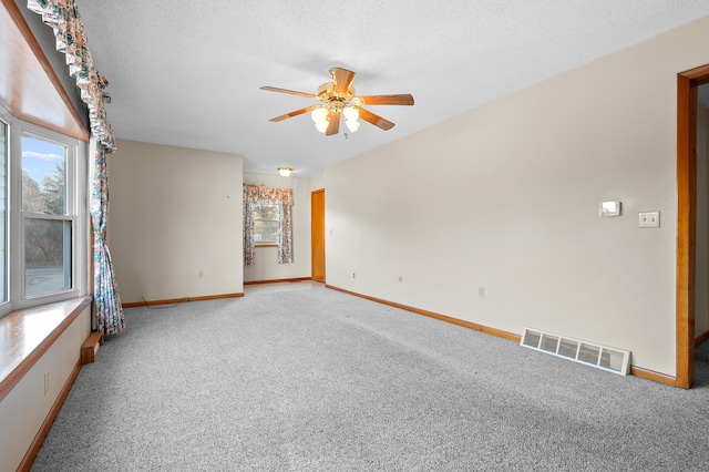 empty room featuring visible vents, light colored carpet, a textured ceiling, and a ceiling fan