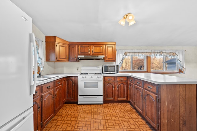 kitchen with white appliances, light countertops, under cabinet range hood, and a sink