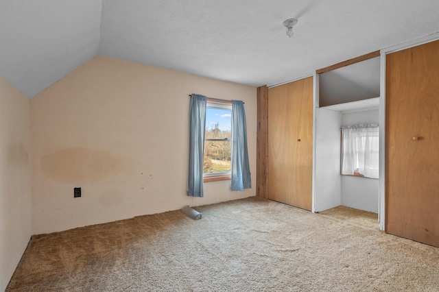 unfurnished bedroom with multiple windows, two closets, lofted ceiling, and carpet floors