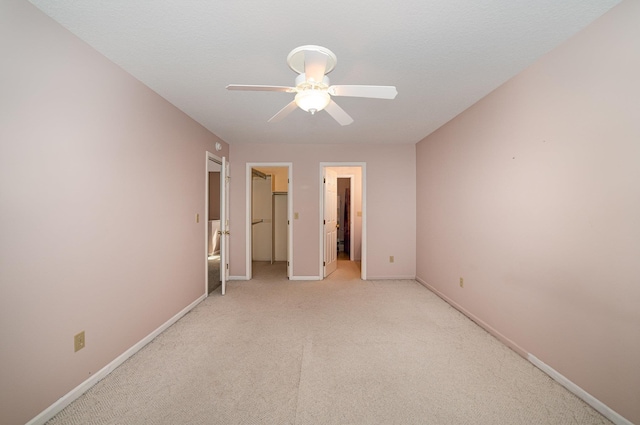 unfurnished bedroom featuring a spacious closet, light colored carpet, baseboards, and ceiling fan