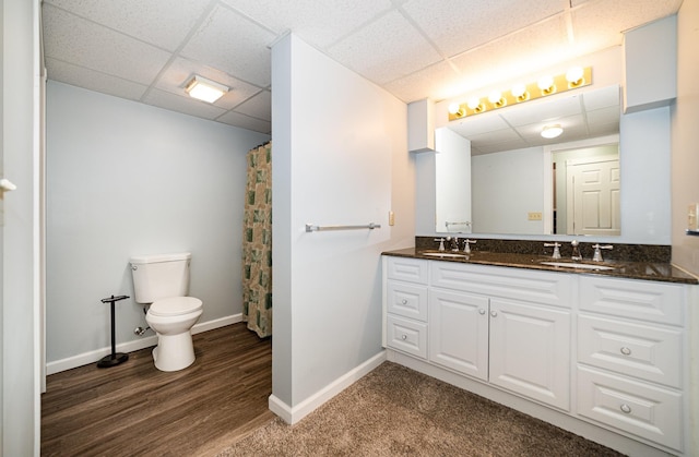 full bath with toilet, a paneled ceiling, baseboards, and a sink