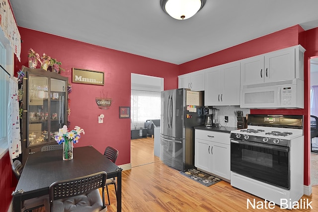 kitchen featuring gas stove, white microwave, freestanding refrigerator, light wood-style floors, and white cabinetry