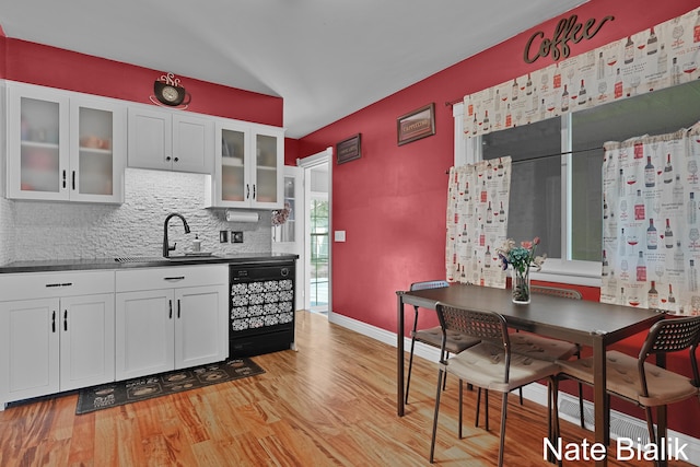 kitchen with a sink, tasteful backsplash, black dishwasher, light wood-style floors, and white cabinets