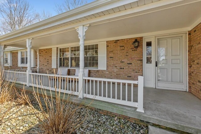 view of exterior entry featuring brick siding and covered porch