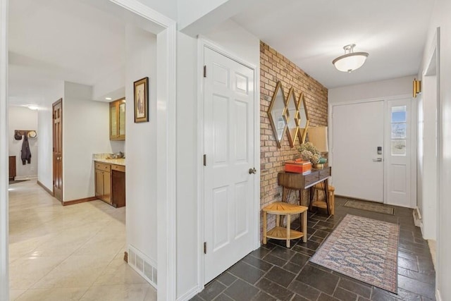 entrance foyer with visible vents, baseboards, brick wall, and stone finish floor