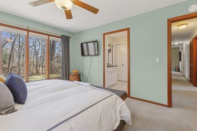 bedroom with ensuite bath, light colored carpet, baseboards, and ceiling fan