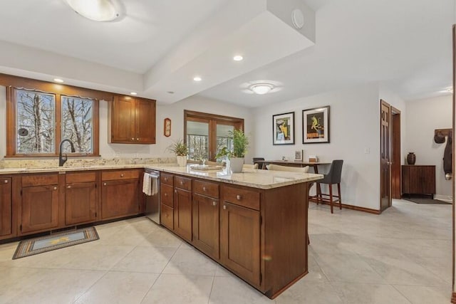 kitchen with baseboards, light stone counters, a peninsula, stainless steel dishwasher, and a sink