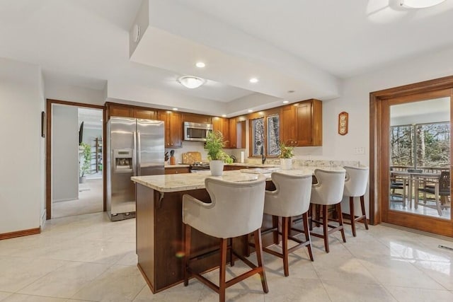 kitchen with a breakfast bar area, baseboards, a peninsula, stainless steel appliances, and brown cabinets