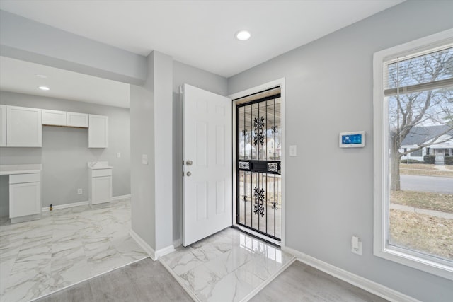 entryway featuring marble finish floor, a healthy amount of sunlight, and baseboards