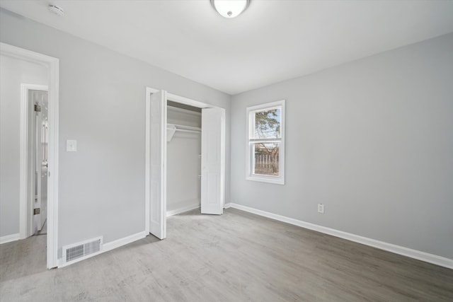 unfurnished bedroom with wood finished floors, visible vents, a closet, and baseboards