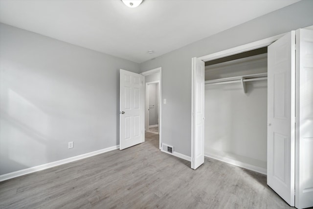 unfurnished bedroom with wood finished floors, visible vents, a closet, and baseboards