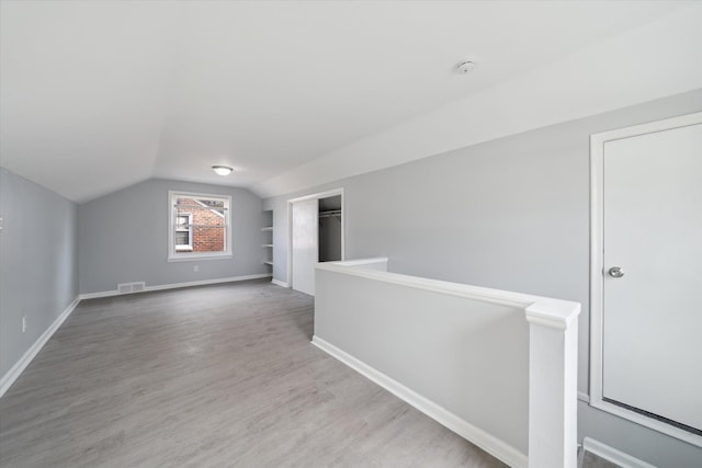 additional living space featuring light wood finished floors, visible vents, baseboards, and lofted ceiling