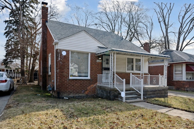 bungalow with covered porch, roof with shingles, a front yard, brick siding, and a chimney