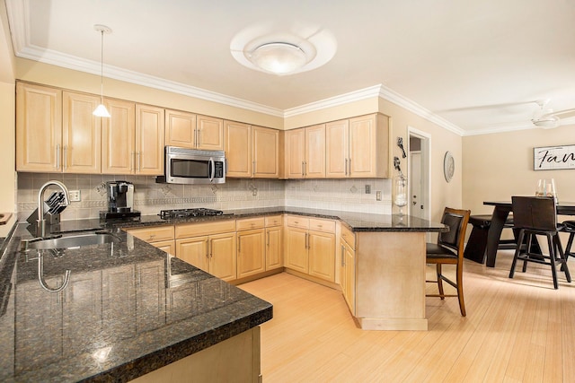 kitchen with light wood-type flooring, light brown cabinets, a sink, a kitchen breakfast bar, and stainless steel appliances