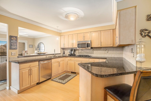 kitchen featuring light wood-style flooring, light brown cabinets, a sink, stainless steel appliances, and a peninsula