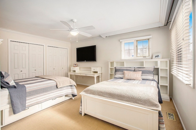 bedroom with visible vents, multiple closets, ornamental molding, light carpet, and a ceiling fan