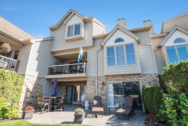 rear view of house featuring brick siding, a balcony, a chimney, and a patio area