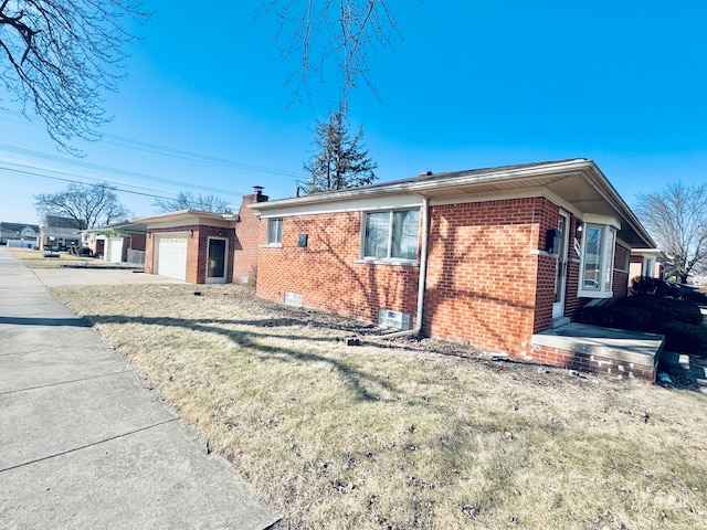 view of side of property featuring brick siding, driveway, an attached garage, and an outbuilding