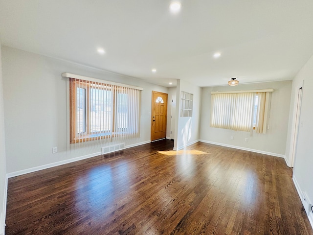 unfurnished living room featuring a wealth of natural light, visible vents, baseboards, and wood finished floors