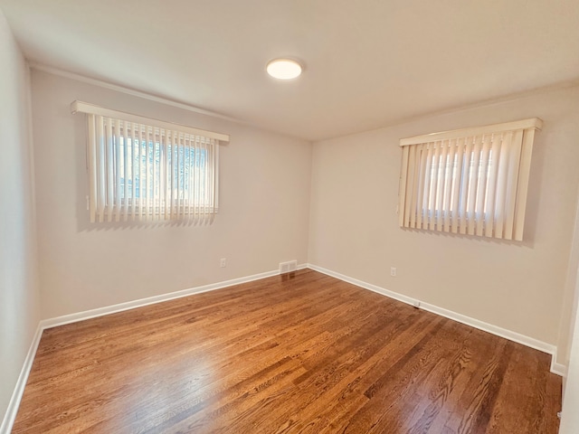 spare room featuring wood finished floors, visible vents, and baseboards