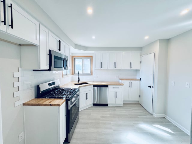 kitchen with a sink, stainless steel appliances, butcher block counters, and white cabinetry