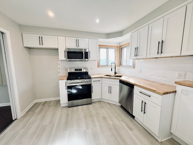 kitchen with backsplash, wooden counters, white cabinets, stainless steel appliances, and a sink