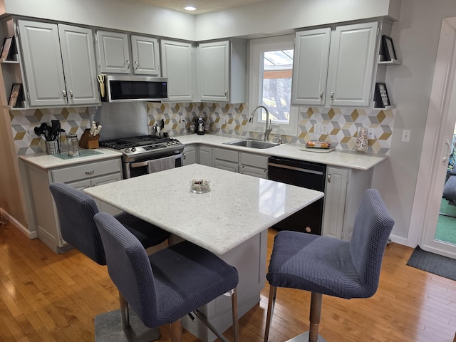 kitchen featuring a breakfast bar, a sink, decorative backsplash, light wood-style floors, and appliances with stainless steel finishes