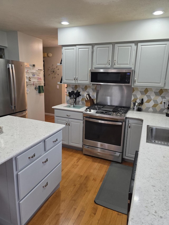 kitchen with light wood-type flooring, appliances with stainless steel finishes, decorative backsplash, and light countertops