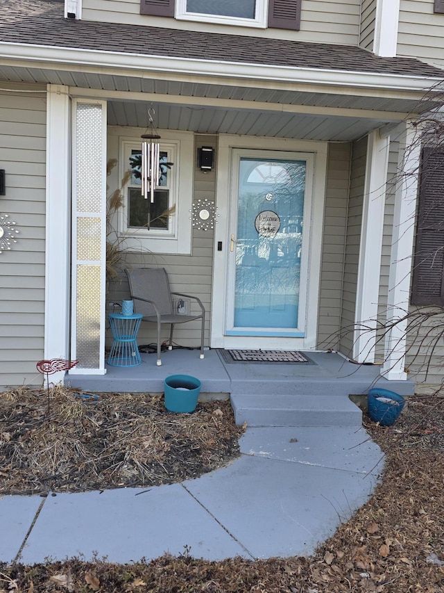 view of exterior entry featuring a porch and a shingled roof