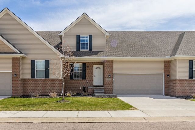 view of front of property with a front yard, driveway, a shingled roof, a garage, and brick siding