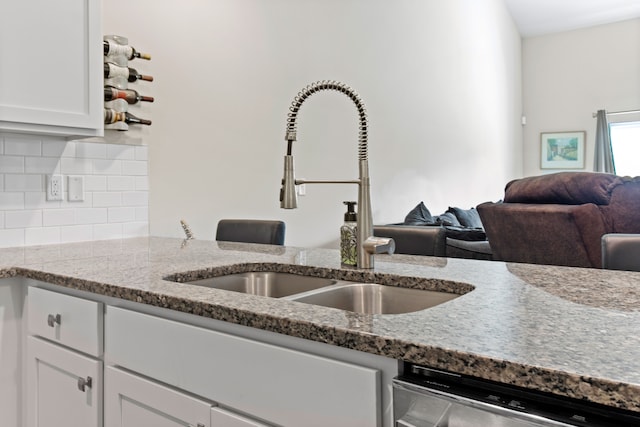 kitchen with a sink, backsplash, light stone countertops, and stainless steel dishwasher