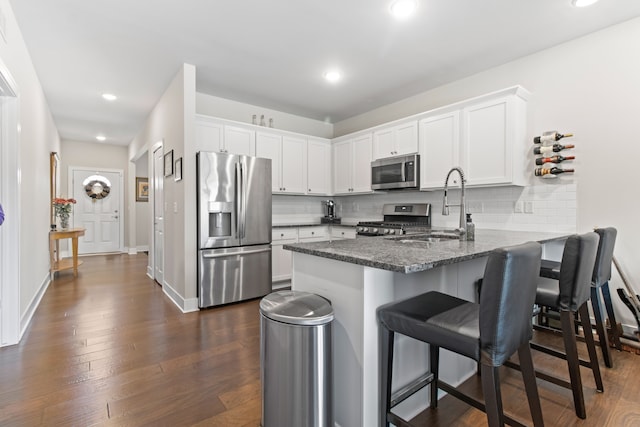 kitchen with appliances with stainless steel finishes, a peninsula, dark wood-style floors, white cabinetry, and a sink