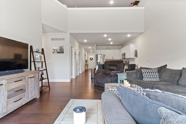 living area with visible vents, a towering ceiling, baseboards, and dark wood-style flooring