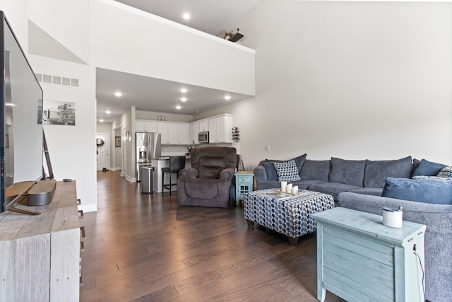 living room with recessed lighting, visible vents, dark wood-style floors, and a towering ceiling