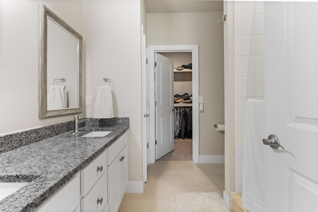 full bath featuring a spacious closet, vanity, a shower, and baseboards