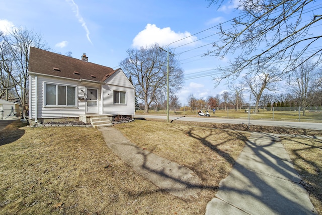 view of front of home with a shingled roof, a front yard, and a chimney