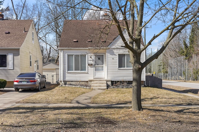 cape cod home featuring an outbuilding, driveway, fence, roof with shingles, and a garage