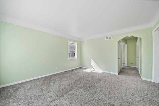 carpeted empty room with visible vents, arched walkways, and baseboards